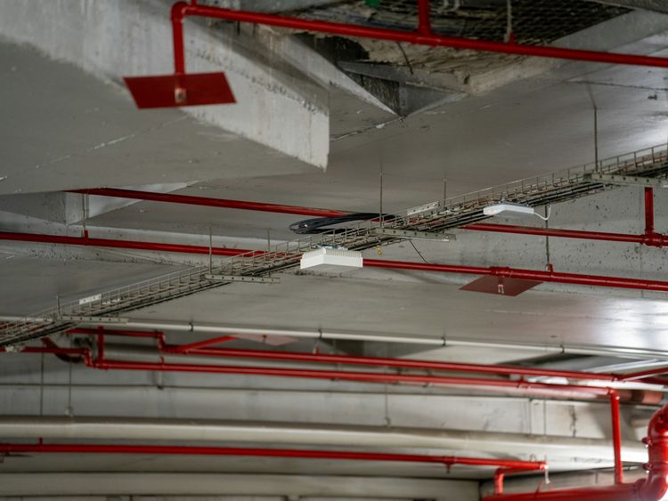 Red service pipes and cable trays under a concrete basement ceiling
