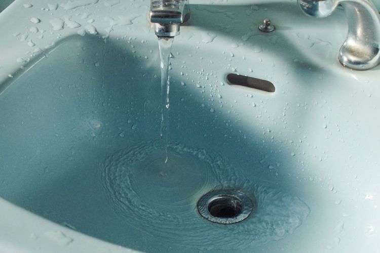 Water from a tap swirling down a basin plughole