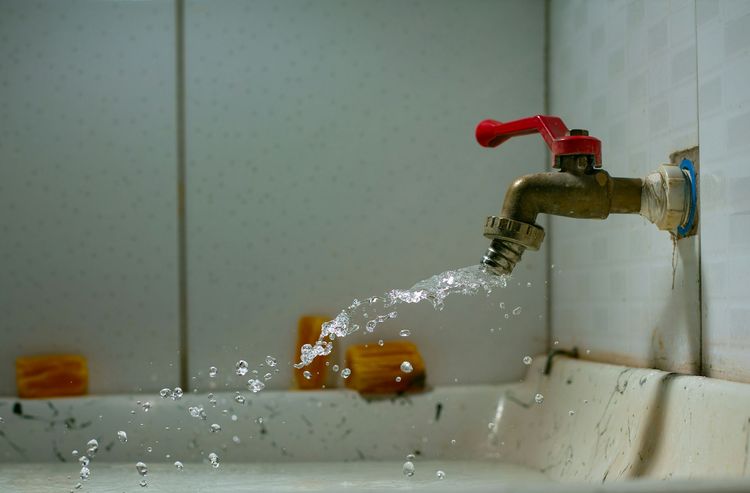 Water gushing from a brass tap with a red lever handle