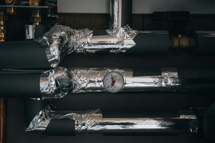 Insulated hot-water pipes wrapped in foil tape, with a pressure gauge in bar