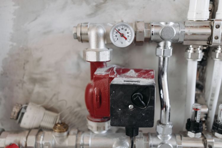 A hot-water circulation pump with a temperature gauge on chrome pipework