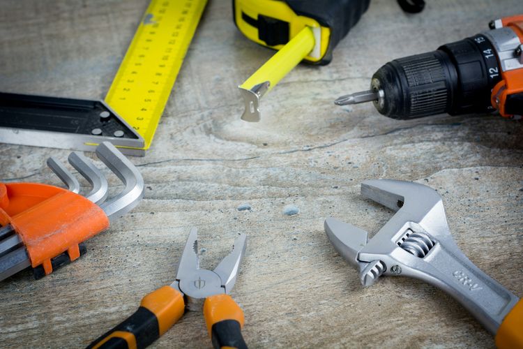 Hand tools laid out on stone: a shifting spanner, pliers, a square, a tape measure and a drill